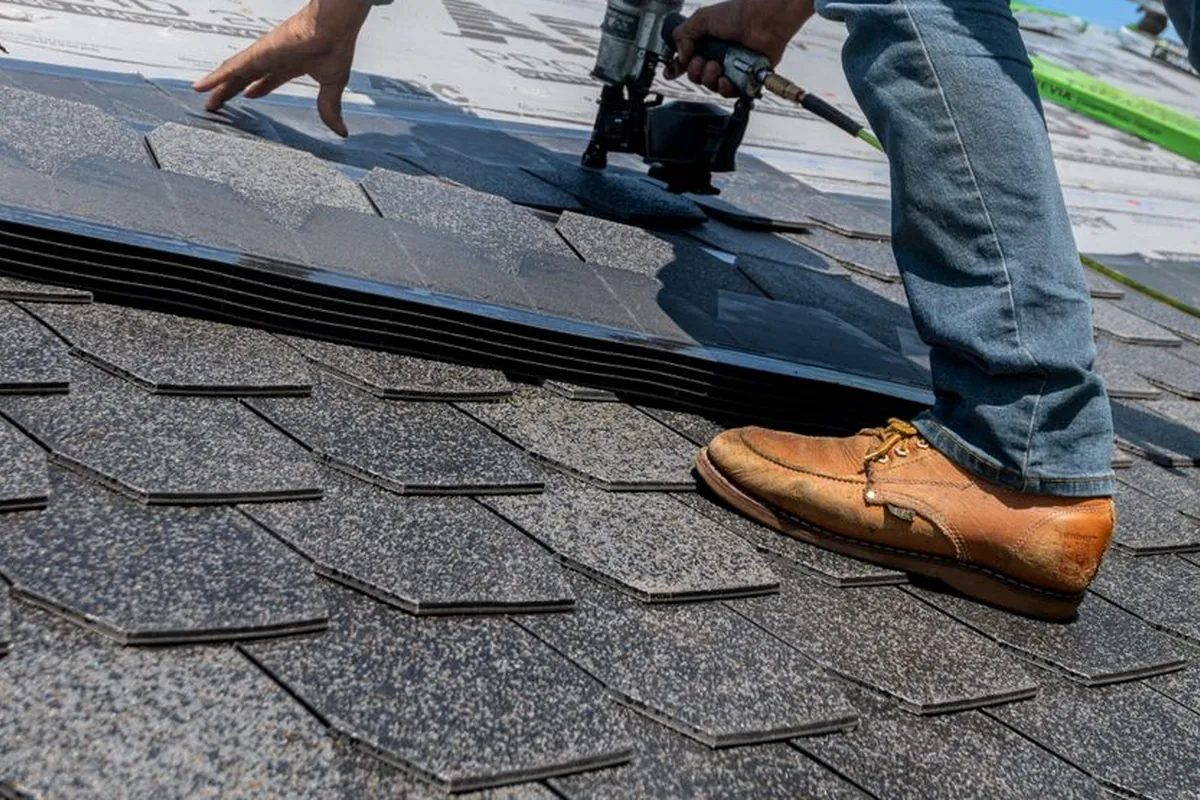 Illustrative roofing workmanship: a roofer fitting overlapping shingles on a pitched roof